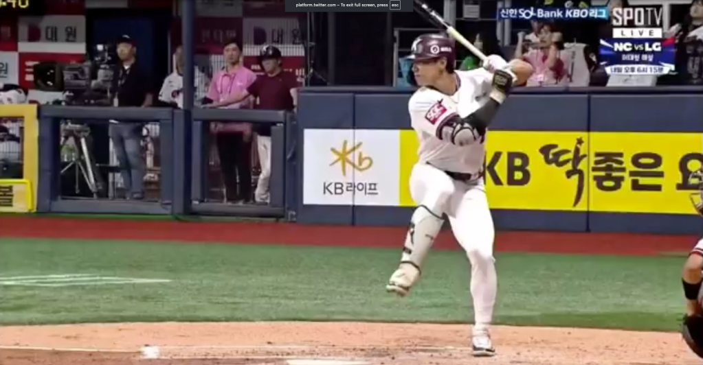 A baseball player in a white uniform with a maroon helmet and a bat in hand, standing at home plate, with "KB" and "KB LIFE" visible on the surrounding signage.